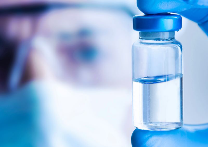 Researcher wearing mask, safety glasses and cap holding a vaccine vial